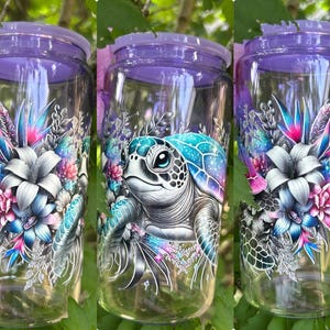 May include: Clear glass jar with a purple lid, featuring a colorful design of a sea turtle and floral elements. The artwork includes shades of blue, pink, and white, creating a vibrant and detailed aesthetic. The jar is surrounded by green foliage.