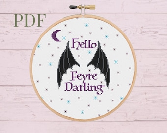 May include: A cross-stitch pattern featuring a crescent moon, a pair of black wings, and the text "Hello Feyre Darling" on a white background with blue and white stars.