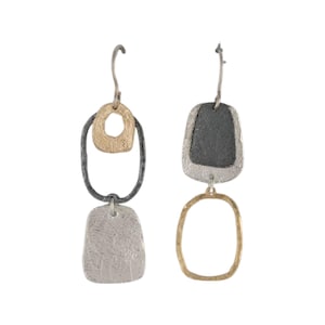 May include: A pair of abstract dangle earrings. One earring features a gold-coloured oval shape connected to a black oval, and a silver-coloured rectangular shape. The other earring has a black top, silver middle, and gold oval bottom.