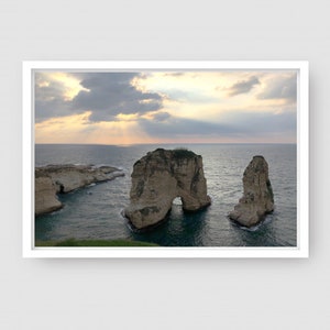 May include: A scenic view of three rock formations jutting out of the ocean. The rocks are a light brown color and are surrounded by blue water. The sky is a light blue with white clouds and sunbeams shining through.