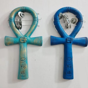 May include: Two Ankh symbols, one blue and one teal, with gold accents. Both have a metal frame with small metal discs that make a sound when shaken. The Ankh symbols have hieroglyphics on the bottom.