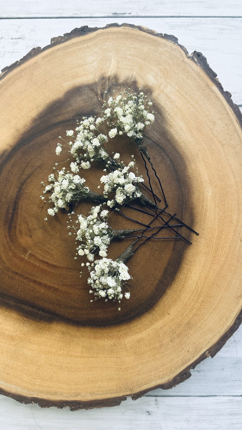 K&ouml;nnte beinhalten: F&uuml;nf wei&szlig;e Baby's Breath Blumenhaarspangen auf einem Holzgrund. Die Spangen sind schwarz und haben eine leichte Biegung am Ende.
