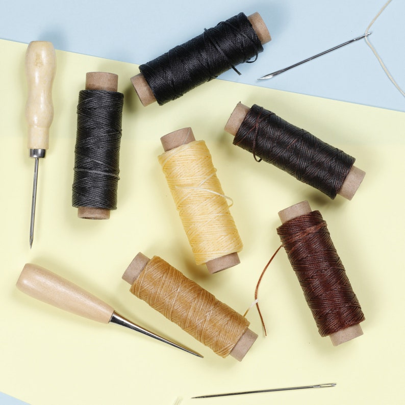 May include: Assortment of six spools of waxed thread in black, brown, beige, and yellow colors. Two awls with wooden handles are also included.