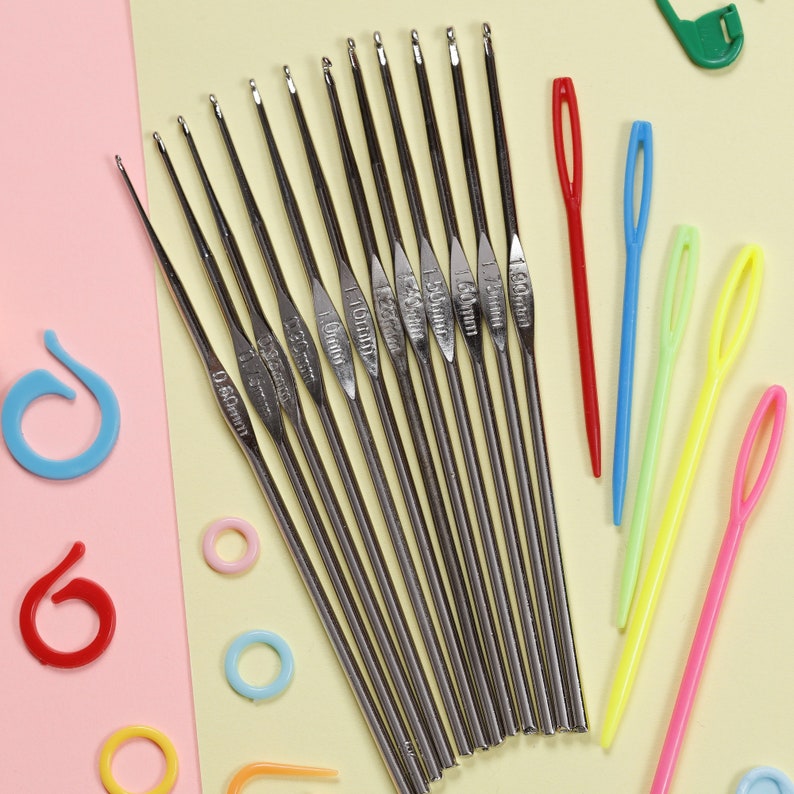 May include: A collection of crochet hooks and yarn needles. The crochet hooks are silver with size markings, ranging from 0.60mm to 1.60mm. Colorful plastic yarn needles and stitch markers in various colors are also included.