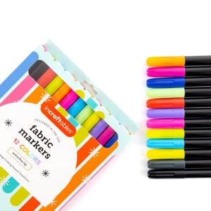 Op de afbeelding: Een set van 12 stoffen stiften in verschillende felle kleuren, waaronder rood, oranje, geel, groen, blauw, paars, roze en zwart. De stiften zijn verpakt in een kleurrijke doos met de tekst "incraftables fabric markers 12 COLORS extra fine tip" erop gedrukt.