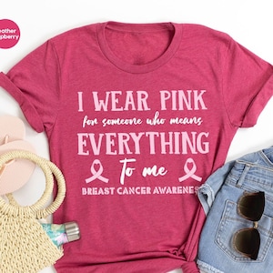 May include: A heather raspberry t-shirt with the text "I wear pink for someone who means everything to me" and a pink ribbon graphic. The text "Breast Cancer Awareness" is also included on the shirt.