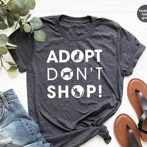 May include: Heather dark grey t-shirt with the text "Adopt Don't Shop!" in white. The text is surrounded by circles with a cat and dog silhouette in each circle.