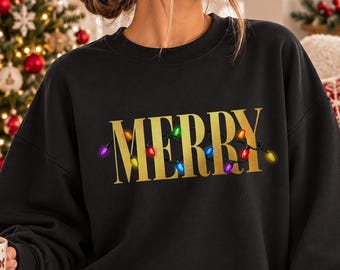 May include: A black crewneck sweatshirt featuring the word MERRY in large gold letters, with a string of colorful Christmas lights wrapped around the text. The sweatshirt has long sleeves and a ribbed collar, cuffs, and hem.