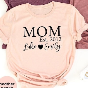 May include: Three t-shirts in different colours with the text "MOM Est. 2012 Luke Emily" on them. The shirts are heather maroon, heather peach, and heather mauve.