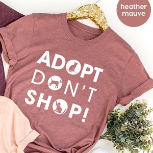 May include: Three t-shirts in different colors with the text "Adopt Don't Shop!" printed on them. The shirts are heather maroon, heather peach, and heather mauve.