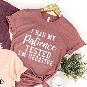 May include: Three t-shirts with the text "I had my patience tested I'm negative" in black and white lettering. The shirts are in different colors: maroon, pink, and a lighter maroon.