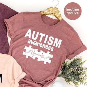 May include: Three t-shirts with the text "AUTISM awareness" and a puzzle piece design. The shirts are in heather maroon, heather peach, and heather mauve.