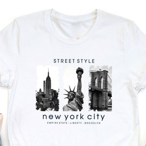 May include: White t-shirt with a black and white graphic print of the New York City skyline, the Statue of Liberty, and the Brooklyn Bridge. The text "STREET STYLE" and "new york city" is printed on the shirt.