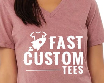 May include: A mauve V-neck t-shirt with a white graphic of a rocket launching a t-shirt with the text "FAST CUSTOM TEES".