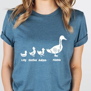 Puede incluir: Una camiseta de color azul oscuro con un gr&aacute;fico blanco de una l&iacute;nea de patos. Los patos est&aacute;n etiquetados como "Lily", "Sasha", "Adam" y "Mama".