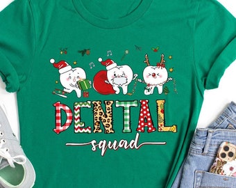 Op de afbeelding: Een kellygroen t-shirt met een afbeelding van drie cartoon-tanden verkleed voor Kerstmis, met de tekst DENTAL squad in patronen. Het ontwerp bevat een tand met een kerstmuts, een tand als de kerstman en een tand als een rendier.