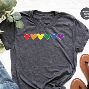 May include: A heather dark grey t-shirt with a row of rainbow coloured hearts across the chest.