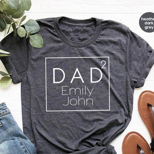 May include: Heather dark grey t-shirt with a white square design that says "DAD&sup2; Emily John".