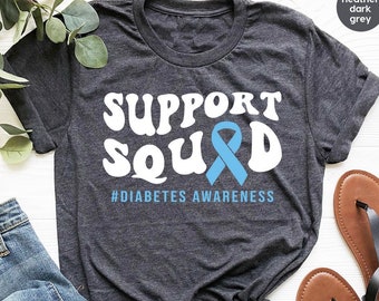 Puede incluir: Una camiseta gris oscuro jaspeada con el texto "SUPPORT SQUAD" en blanco con una cinta azul y el texto "#DIABETES AWARENESS" en negro.