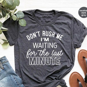 May include: A heather dark grey t-shirt with the text "DON'T RUSH ME I'M WAITING for the last MINUTE" printed in white.
