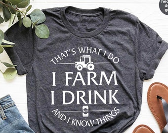 May include: A heather dark grey t-shirt with a white graphic that says "That's what I do I farm I drink and I know things". The graphic also includes a cartoon tractor and a beer can.