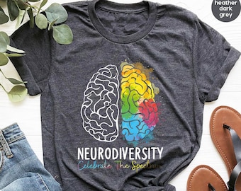 May include: Heather dark grey t-shirt with a graphic of a brain with one half in black and white and the other half in rainbow colors. The text "Neurodiversity Celebrate The Spectrum" is printed below the graphic.