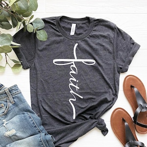 May include: A dark gray t-shirt with a white cross and the word "faith" written vertically down the cross.