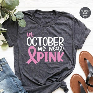 Pu&ograve; includere: Una maglietta color grigio scuro melange con il testo "in OCTOBER we wear PINK" e una grafica a nastro rosa.