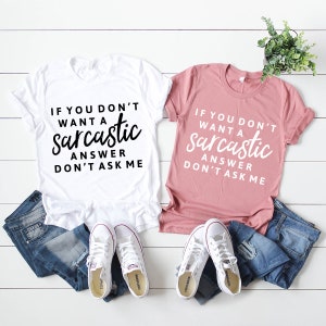 May include: Two t-shirts with the text "If you don't want a sarcastic answer don't ask me" on them. One shirt is white with black text and the other is pink with white text.