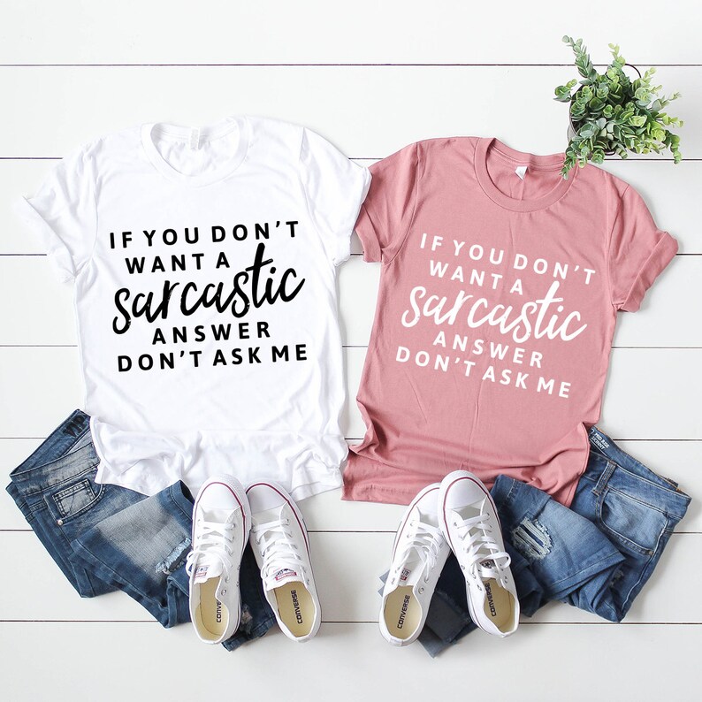 May include: Two t-shirts with the text "If you don't want a sarcastic answer don't ask me" on them. One shirt is white with black text and the other is pink with white text.