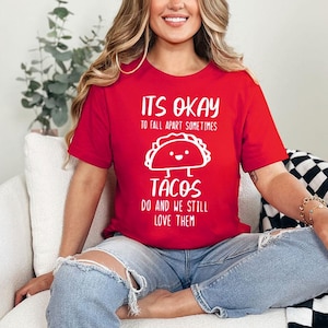 May include: Red t-shirt with white text that reads "It's okay to fall apart sometimes tacos do and we still love them". The shirt features a cartoon taco with a happy face.