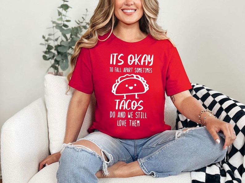 May include: Red t-shirt with white text that reads "It's okay to fall apart sometimes tacos do and we still love them". The shirt features a cartoon taco with a happy face.
