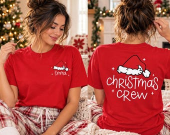 May include: A red short-sleeved t-shirt featuring a white graphic of a Santa hat and the name Emma on the front left chest, and a larger white graphic of a Santa hat with the text Christmas Crew on the back.