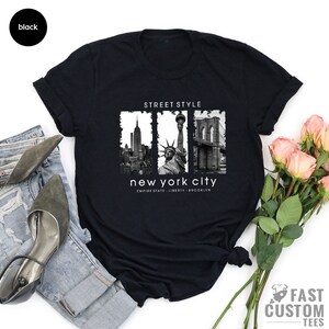 May include: Black t-shirt with a graphic of the New York City skyline, including the Empire State Building, the Statue of Liberty, and the Brooklyn Bridge. The text "Street Style" and "New York City" is printed on the shirt.