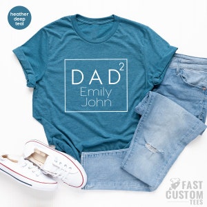 May include: A teal blue t-shirt with a white square graphic that says "DAD&sup2; Emily John" on it.