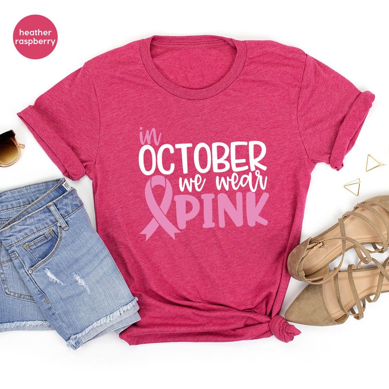 Pu&ograve; includere: Una t-shirt color lampone heather con il testo "in OCTOBER we wear PINK" e una grafica a nastro rosa.