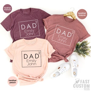 May include: Three t-shirts with the text "DAD&sup2;" and the names "Emily John" printed on them. The shirts are in different colors: heather maroon, heather mauve, and heather peach.