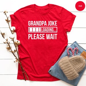 May include: Red t-shirt with white text that reads "Grandpa Joke Loading... Please Wait".