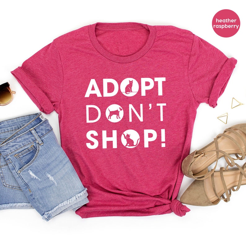 May include: Heather raspberry t-shirt with the text "Adopt Don't Shop!" in white. The text is surrounded by circles with a cat and dog silhouette inside each circle.