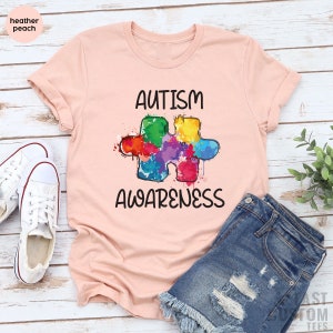 May include: A pink t-shirt with the words "AUTISM AWARENESS" and a colorful puzzle piece graphic.