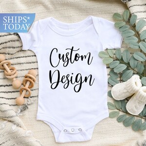 May include: White baby onesie with black text that reads "Custom Design".