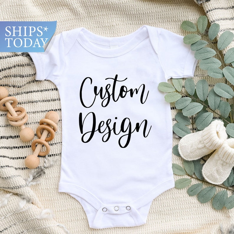 May include: White baby onesie with black text that reads "Custom Design".