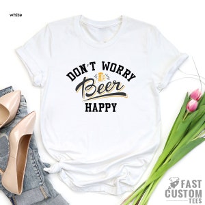May include: White t-shirt with black text that reads "Don't Worry Beer Happy" with a beer mug graphic.