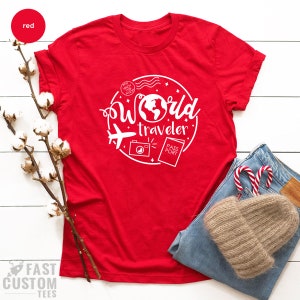 May include: Red t-shirt with a white graphic design that says "World Traveler" with a globe, airplane, camera, and passport.