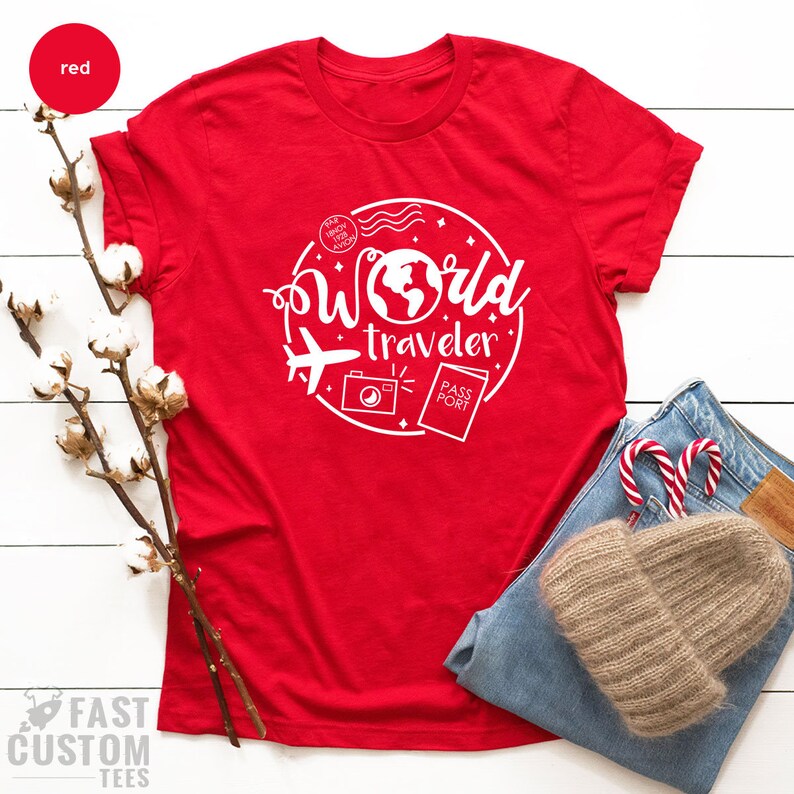 May include: Red t-shirt with a white graphic design that says "World Traveler" with a globe, airplane, camera, and passport.