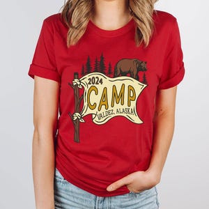 a woman wearing a red shirt with a camp sign on it