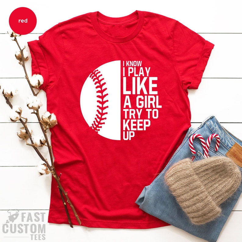 Op de afbeelding: Rood T-shirt met een witte baseball-afbeelding en de tekst "I know I play like a girl try to keep up".