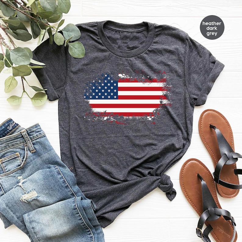 Peut inclure: Un t-shirt gris fonc&eacute; chin&eacute; avec un motif de drapeau am&eacute;ricain d&eacute;lav&eacute;. Le drapeau est rouge, blanc et bleu.