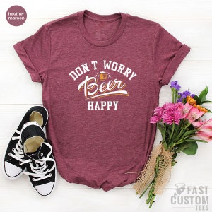 May include: Heather maroon t-shirt with the text "Don't Worry, Be Happy" in white with a beer mug graphic in orange.
