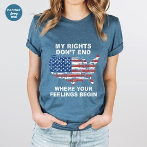 May include: Teal t-shirt featuring the text "MY RIGHTS DON'T END WHERE YOUR FEELINGS BEGIN" and a graphic of the USA flag in the shape of the United States. The shirt has short sleeves and a crew neck.